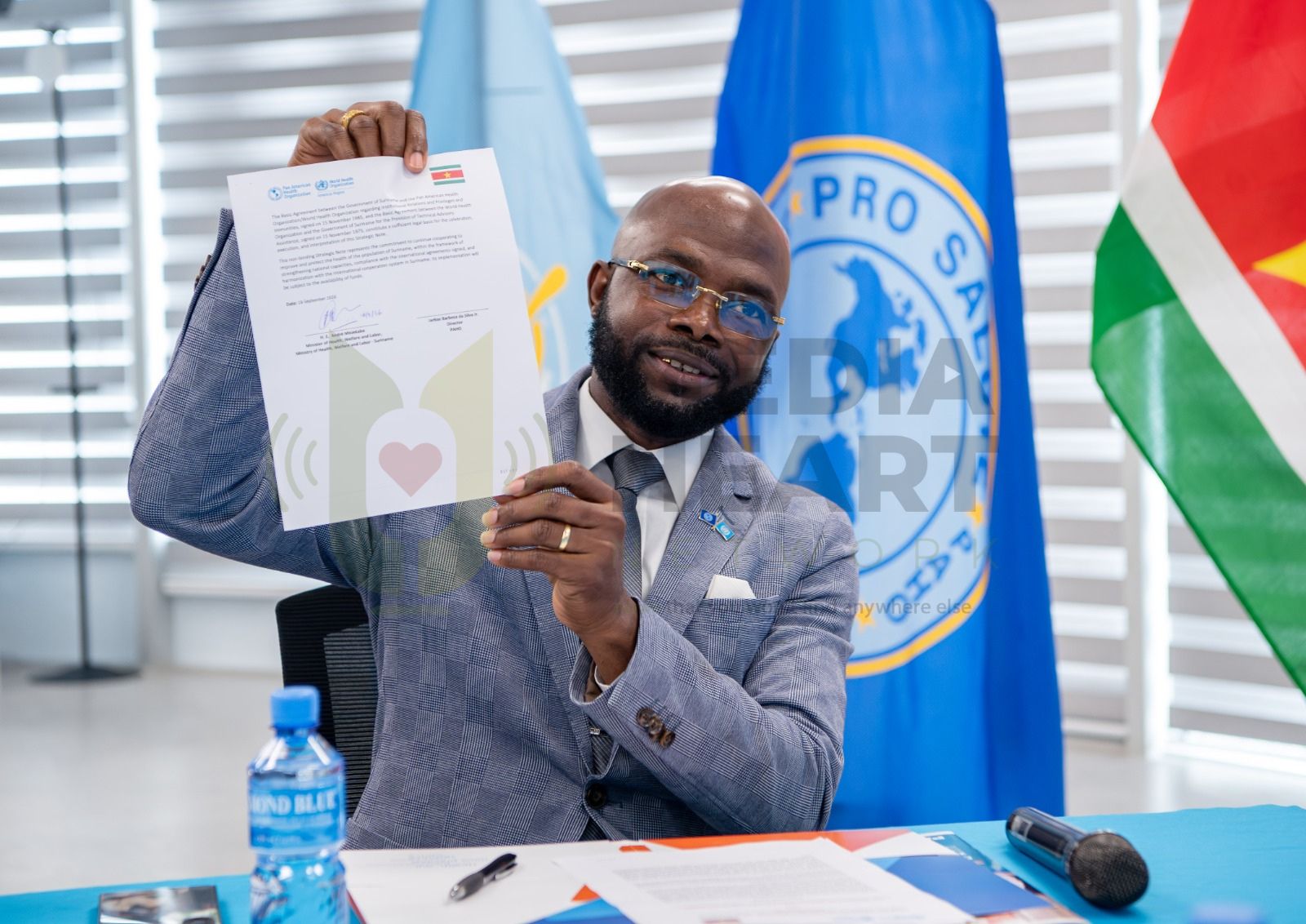 Minister André Misiekaba laat breed lachend het MoU zien die is getekend met de PAHO