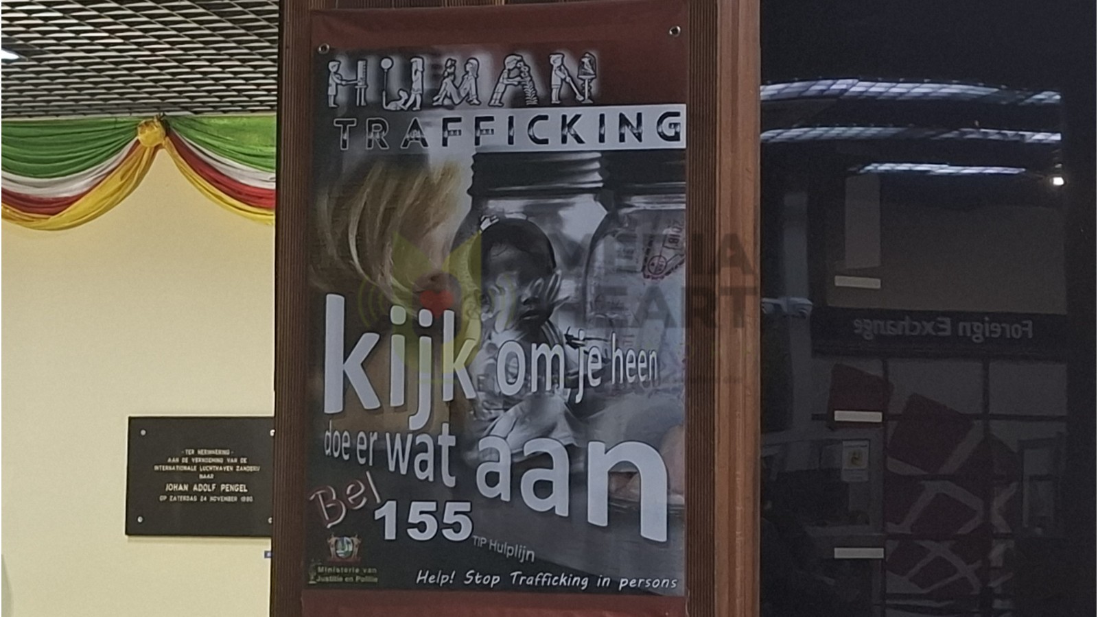 Deze banner staat op de JAP Luchthaven om personen bewust te maken van mensenhandel en mensensmokkel
